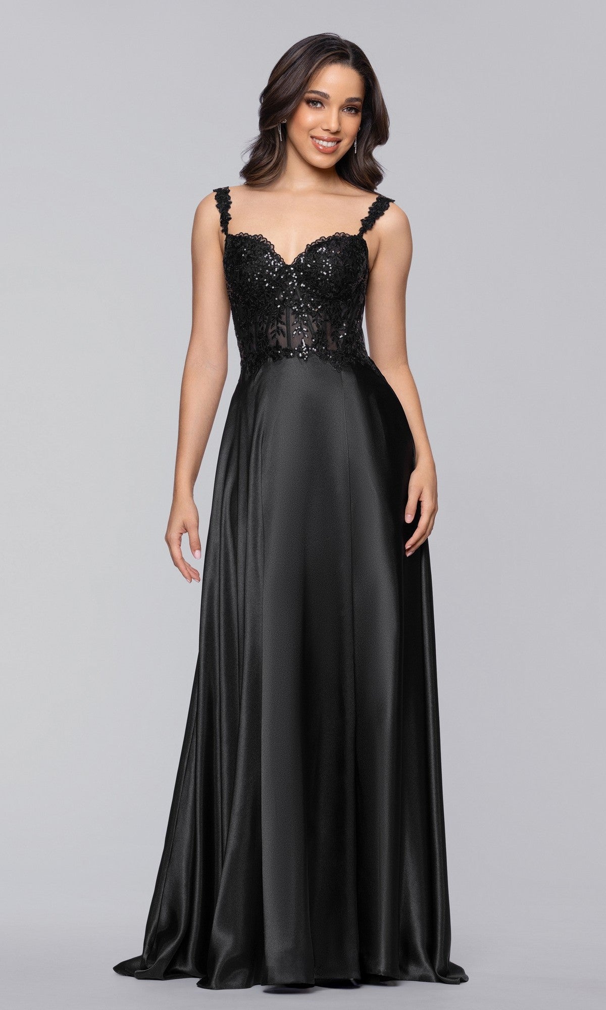 A woman stands against a plain light background wearing the Long Prom Dress: Blondie Nites 6088BN—an A-line black satin gown with a sequin-embellished bodice, lace straps, and a long flowing skirt.